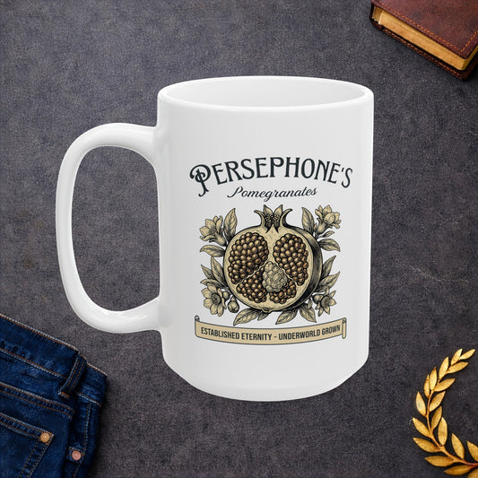 White ceramic mug with a vintage-style botanical illustration of a halved pomegranate showing its seeds, surrounded by delicate pomegranate flowers and leaves. Above the fruit, the text "PERSEPHONE'S Pomegranates" is written in a mix of serif and script fonts. A banner at the bottom reads "ESTABLISHED ETERNITY - UNDERWORLD GROWN." The design features an elegant, woodcut aesthetic in muted earthy tones.