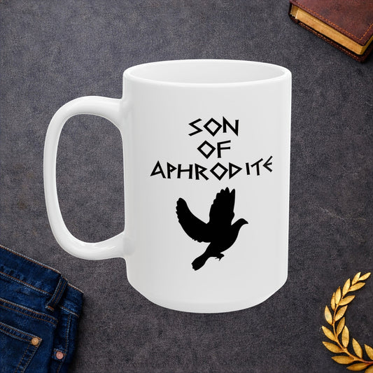 White ceramic mug featuring a minimalist, Greek-inspired graphic in black ink on a white background. The design reads 'SON OF APHRODITE' in a stylized, angular font, positioned above a clean, line-art graphic of a dove in flight.