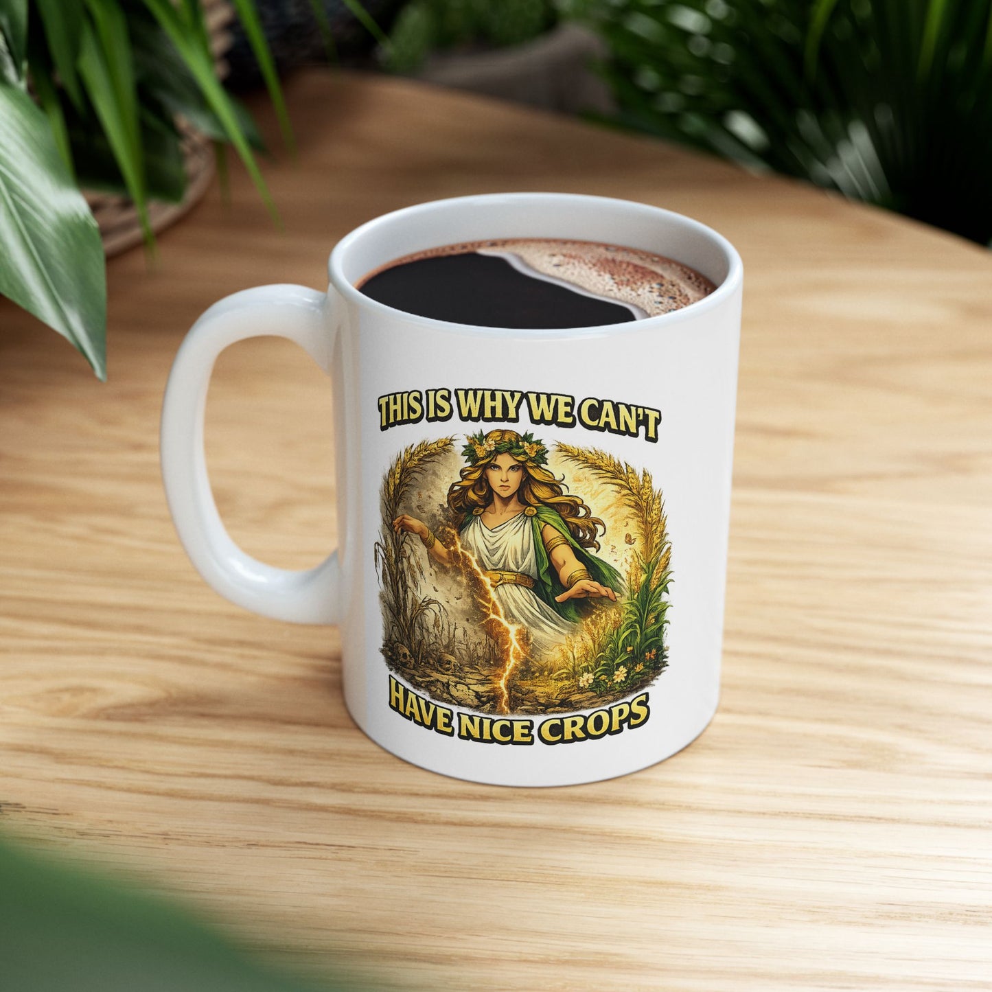 White ceramic mug with a dramatic illustration of Demeter, the Greek goddess of agriculture, standing over a split field. A glowing lightning strike cracks down the center, dividing flourishing, green crops on the right from dead, withered stalks and skulls on the left. Arching text above and below reads "THIS IS WHY WE CAN'T HAVE NICE CROPS" in a bold, weathered yellow font. The design has an intense, mythical comic art style.