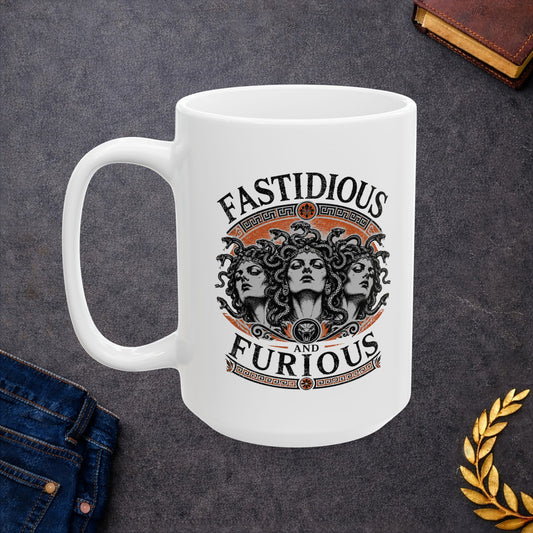 White ceramic mug with a Humorous design combining 'Fast and Furious' with Greek mythology on a white ceramic mug. Text reads 'FASTIDIOUS AND FURIOUS' in distressed lettering surrounding three faces of Medusa in black and white engraving style. Detailed serpents with individual scales form her hair. Greek key pattern borders in orange frame the composition with decorative sun motifs and a small snake head icon at center. Blends classical mythology with contemporary pop culture humor.