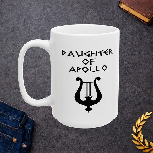 White ceramic mug featuring a minimalist, Greek-inspired graphic in black ink on a white background. The design reads 'DAUGHTER OF APOLLO' in a stylized, angular font, positioned above a clean, line-art graphic of a classical lyre.