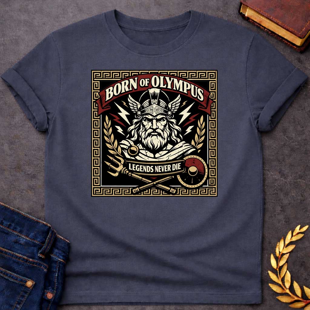 Dark Heather T-shirt graphic featuring a bold vintage label-style design with a Greek meander border in gold. A red arched banner at the top reads "Born of Olympus" above a front-facing illustration of Zeus with long white hair and beard wearing a winged helmet, surrounded by radiating lightning bolts and flanked by golden laurel branches. A crossed trident and scepter with a red shield sit below, with a scroll banner reading "Legends Never Die," rendered in black, gold, cream, and red tones