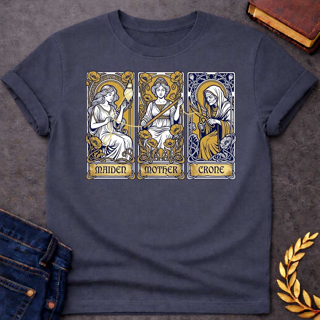 Dark Heather T-shirt graphic featuring three Art Nouveau-style tarot card panels in navy, gold, and white, each depicting one of the Moirai, the Greek Fates, as the triple goddess archetypes. The first panel shows the Maiden as a young woman spinning a golden thread from a spindle amid poppies, labelled "Maiden." The middle panel shows the Mother as a composed woman measuring the thread with a ruler surrounded by blooming poppies, labelled "Mother." The third panel shows the Crone as an elderly hooded woman