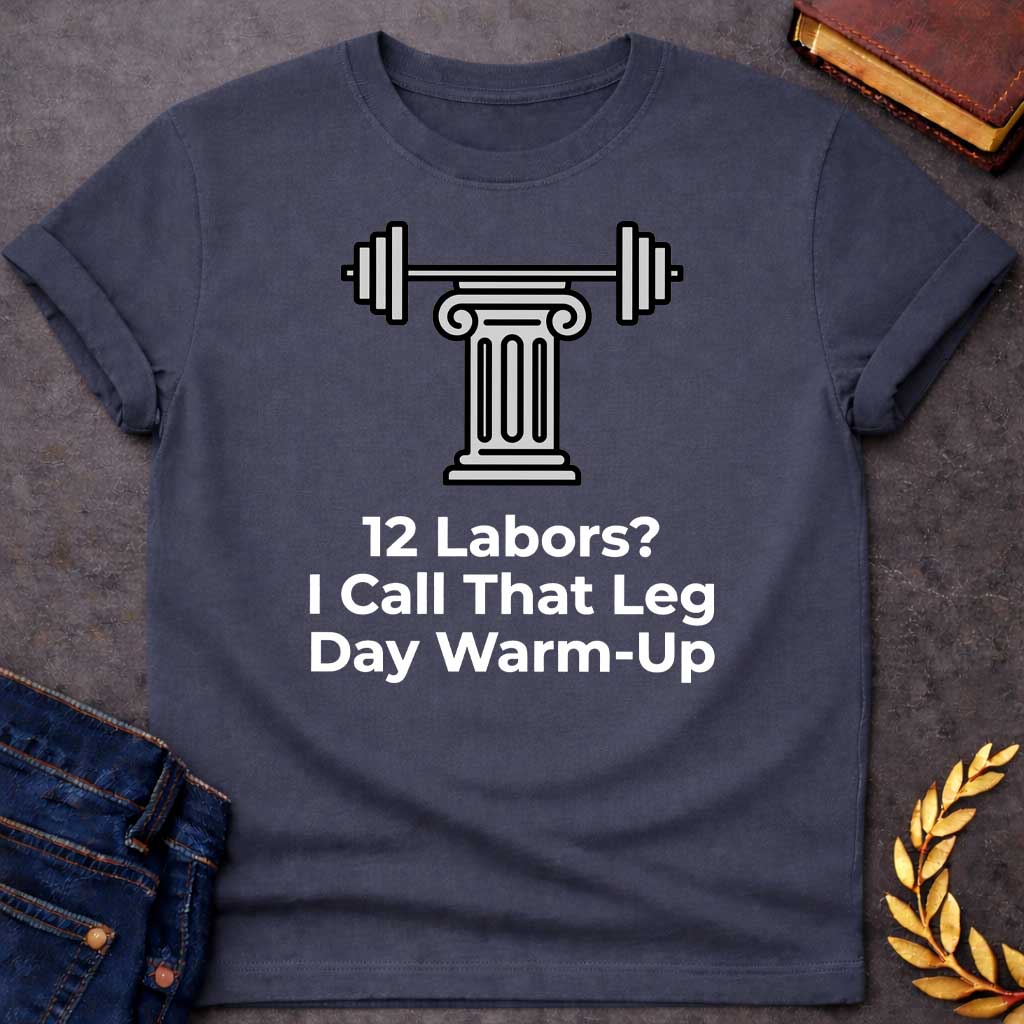 Dark Heather T-shirt with a graphic design. At the top, there is a gray illustration of a classical Greek column supporting a barbell with weight plates on both sides. Below the illustration, the white text reads: "12 Labors? I Call That Leg Day Warm-Up"