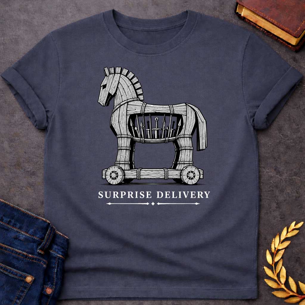 Dark Heather T-shirt with a graphic in black and white featuring a highly detailed realistic ink illustration of the Trojan Horse constructed from weathered wood planks bound with rope on a wheeled platform, with spears and a sword visibly hidden inside its hollow body. Elegant spaced serif text below with decorative arrow dividers reads "Surprise Delivery" — a humorous reference to the Greek legend of the Trojan War