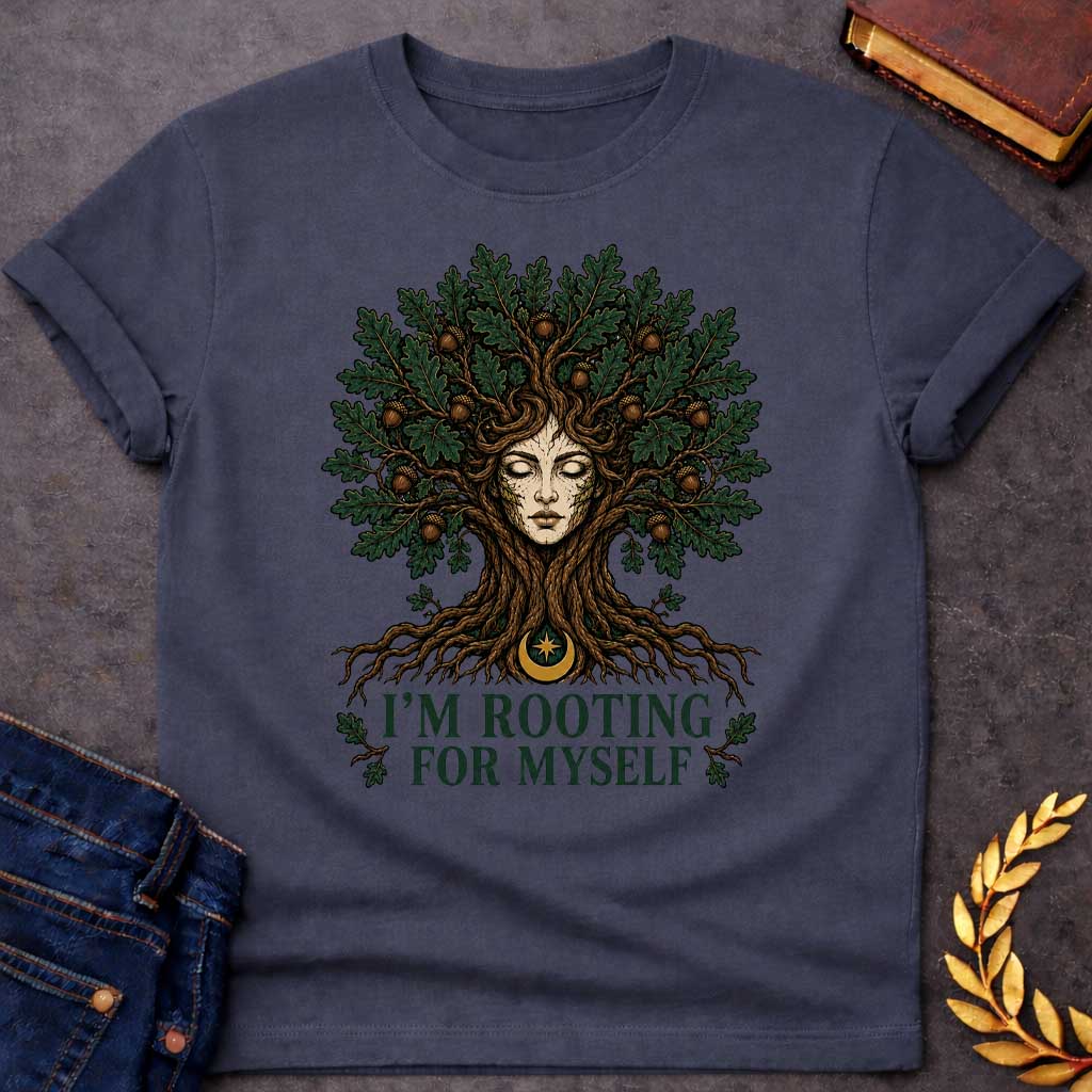 Dark Heather T-shirt with a cottagecore-style graphic featuring a detailed illustration of an oak tree dryad or nature spirit. Her serene, closed-eyed face forms the center of the tree trunk, with gnarled roots expanding below and a massive canopy of dark green oak leaves and brown acorns spreading above. Underneath the roots, a pun-based tagline reads "I'M ROOTING FOR MYSELF" in a bold, clean green serif font.