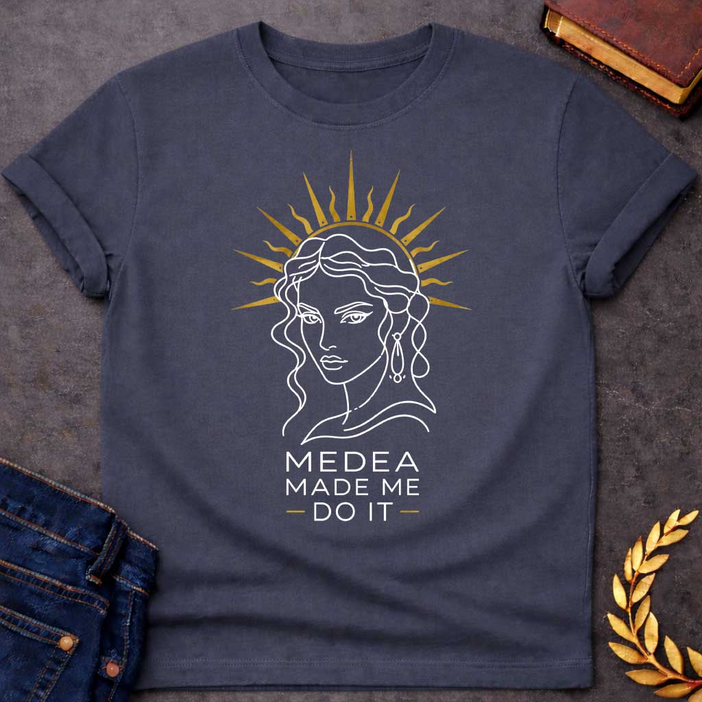 Dark Heather T-shirt with a Minimalist line art portrait of Medea with wavy hair and drop earrings, framed by a golden radiating sun halo. Black and white design with gold accents. Text reads 'Medea Made Me Do It.' Humorous reference to blaming the legendary Greek sorceress for chaotic or destructive actions. Celebrates Medea's infamous power and magical influence with tongue-in-cheek blame attribution.