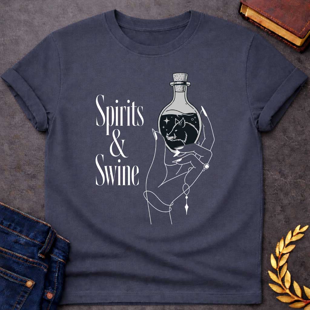 Dark Heather T-shirt with a Minimalist line art illustration of a mystical hand holding a potion bottle labeled 'Spirits & Swine.' Inside the dark bottle, a pig silhouette appears amid glowing stars and magical elements. The elegant hand wears decorative bracelets and rings. Black and white aesthetic with witchy, occult vibes. References Circe's legendary enchanted spirits that transformed men into swine. Celebrates ancient magic, potion-making, and mythological transformation with modern witchcraft themes.