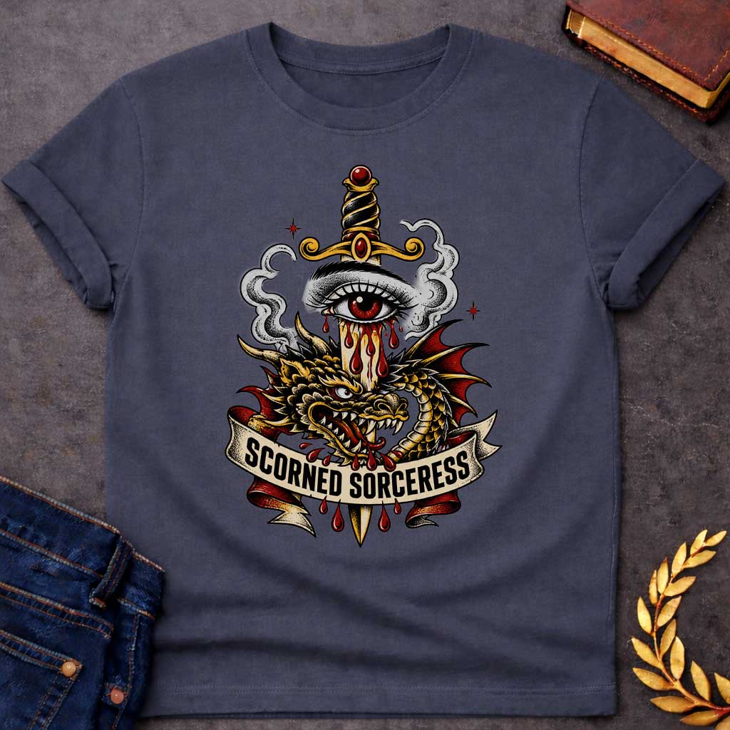 Dark Heather T-shirt featuring traditional tattoo-style artwork: a gold-hilted dagger with black-and-gold wrapped handle and ruby pommel pierces through a weeping red-irised eye, blood streaming down the blade. A gold and red dragon coils around the dagger, fangs bared, with grey smoke curling behind. A cream ribbon banner below reads "Scorned Sorceress" in bold black lettering, dripping blood, on a white background.