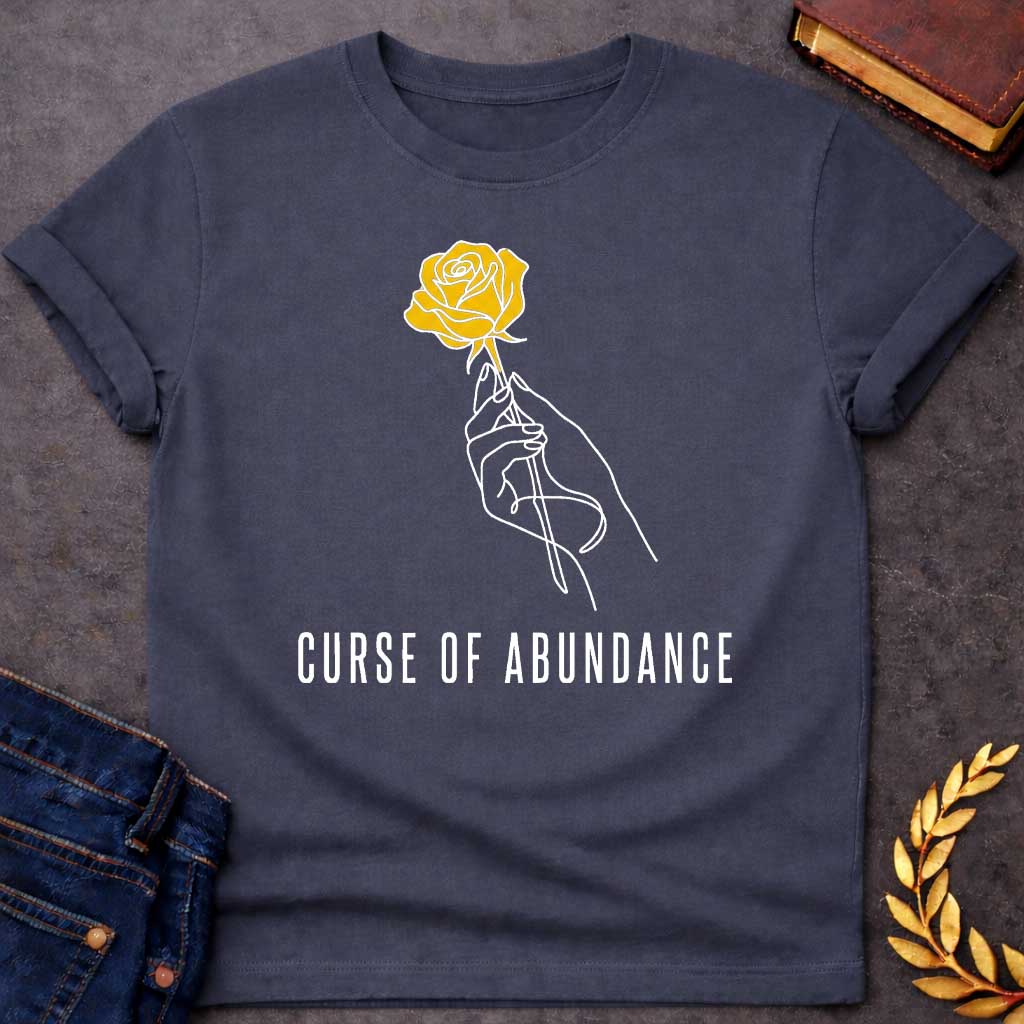 Dark Heather t-shirt with A Minimalist Greek mythology design featuring a continuous line-art hand delicately holding a golden rose, symbolizing King Midas' legendary golden touch. Below the illustration, the phrase "Curse of Abundance" appears in clean, modern typography. A simple black-and-gold aesthetic creates an elegant, understated design inspired by the tragic Midas myth.