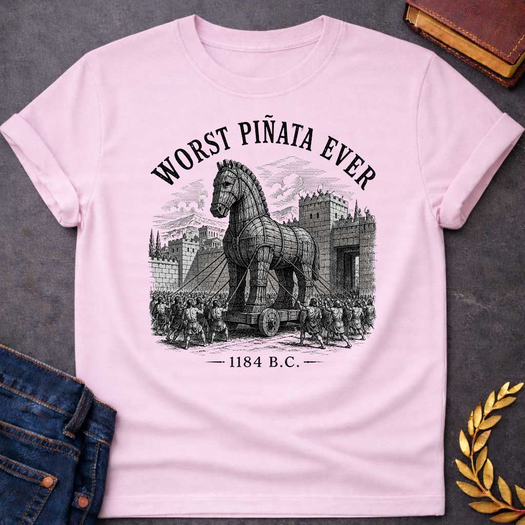 Light Pink T-Shirt with a detailed, woodcut-style graphic design. The central illustration depicts the wooden Trojan Horse being pulled on a wheeled platform by many figures using ropes toward the stone gates of a walled city. Arched over the top of the scene in a distressed, black serif font is the text "WORST PIÑATA EVER." At the bottom of the design, the year "1184 B.C." is printed between two horizontal decorative dashes