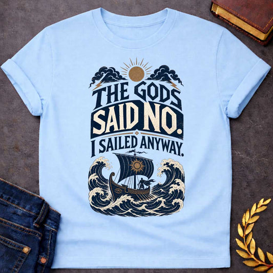 Light Blue t-shirt with a Vintage Greek mythology design featuring the bold phrase “The Gods Said No. I Sailed Anyway.” An ancient Greek ship battles towering ocean waves beneath storm clouds, lightning bolts, and a glowing sun. Distressed navy, cream, and gold artwork captures the defiant spirit of Odysseus and The Odyssey.
