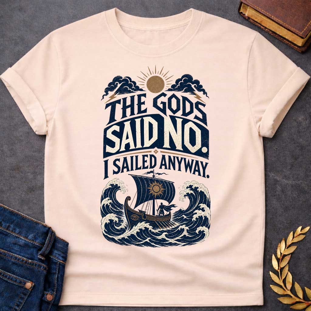 Natural t-shirt with a Vintage Greek mythology design featuring the bold phrase “The Gods Said No. I Sailed Anyway.” An ancient Greek ship battles towering ocean waves beneath storm clouds, lightning bolts, and a glowing sun. Distressed navy, cream, and gold artwork captures the defiant spirit of Odysseus and The Odyssey.