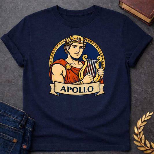 Navy T-shirt graphic featuring a vibrant illustrated portrait of Apollo, the Greek God of the Sun and Music, with short curly hair and a gold laurel crown, wearing a red draped robe fastened with a gold brooch, playing a golden lyre. He is framed within a gold circular border against a navy background, with a scroll banner below reading "Apollo," in a bold tattoo-inspired style with navy, gold, and red tones