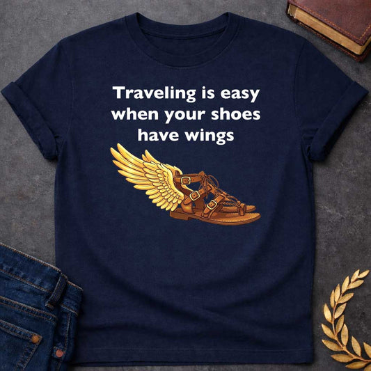 Navy T-shirt graphic featuring bold white text reading "Traveling is easy when your shoes have wings" above a detailed illustration of Hermes' winged sandal, depicted as a brown leather gladiator sandal with gold buckles and braided lacing, with a large golden wing extending from the ankle — a humorous reference to the talaria, the iconic flying sandals of Hermes, the Greek Messenger God