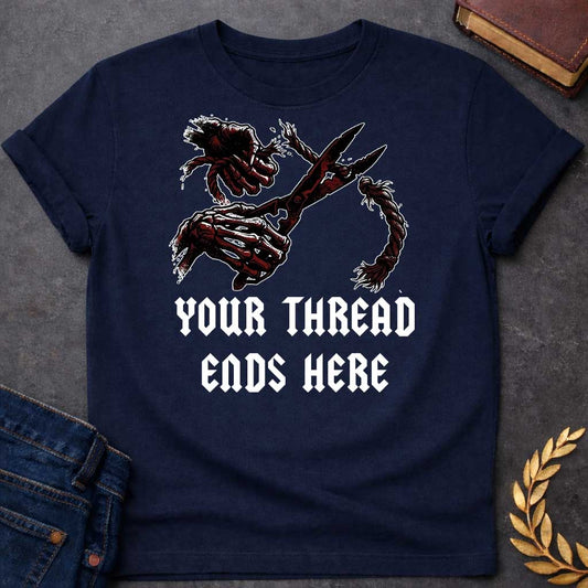 Navy T-shirt graphic in black, white, and dark red featuring a dark illustrated scene of two skeletal hands gripping large shears cutting through a thick fraying rope or thread, rendered in a gritty horror-influenced ink style with ink splatter details. Bold heavy metal-style blackletter text below reads "Your Thread Ends Here" — a dark and dramatic reference to Atropos, the eldest of the Moirai, the Greek Fate who cuts the thread of life