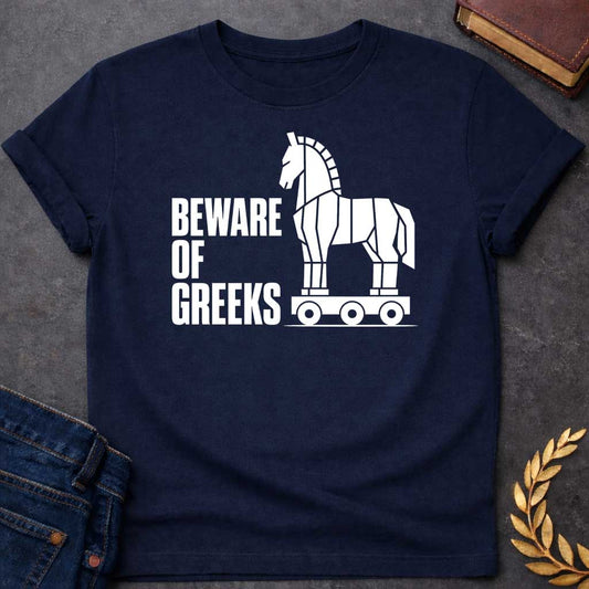 Navy T-shirt with a graphic in white featuring bold condensed sans-serif text reading "Beware of Greeks" alongside a flat geometric white silhouette illustration of the Trojan Horse mounted on a wheeled platform — a humorous reference to the Greek legend of the Trojan War