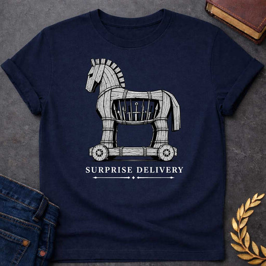 Navy T-shirt with a graphic in black and white featuring a highly detailed realistic ink illustration of the Trojan Horse constructed from weathered wood planks bound with rope on a wheeled platform, with spears and a sword visibly hidden inside its hollow body. Elegant spaced serif text below with decorative arrow dividers reads "Surprise Delivery" — a humorous reference to the Greek legend of the Trojan War