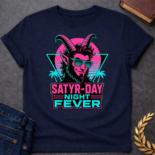 Navy T-shirt with a vibrant 1980s synthwave-style graphic for "satry-day night fever.jpg". It features a cool satyr with large horns, a smirk, and cyan shutter shades, illuminated in neon pink and black. The background shows a retrowave sunset grid, a black triangle, and palm trees. Below, the punny title "SATYR-DAY NIGHT FEVER" is displayed in bold neon pink and cyan block lettering against a dark badge