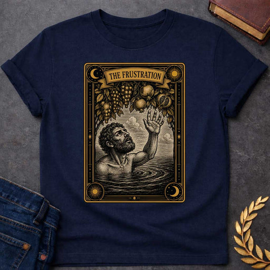 Navy t-shirt with A detailed tarot card-style illustration. Set within an ornate black and gold border featuring sun and moon corner emblems, a bearded man in rippling water reaches one hand up toward hanging branches overflowing with grapes and pomegranates. A ribbon banner across the top of the card displays the title "THE FRUSTRATION" in a bold serif typeface.