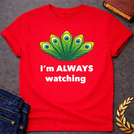 Red T-shirt graphic featuring a vibrant illustrated fan of five peacock feathers in rich green, yellow, and blue tones, each with a distinctive eye-spot, above text reading "I'm Always Watching" — a humorous reference to Hera, the Greek Queen of the Gods, whose sacred symbol is the peacock