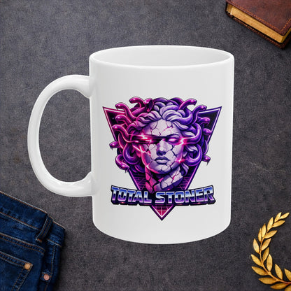 White ceramic mug with a synthwave-inspired graphic of Medusa with purple snakes for hair and a cracked stone face. Glowing pink light emanates from her eyes and cracks. The head is centered over a neon pink and purple triangle with a retro grid. Below, the pun "TOTAL STONER" is written in a 1980s-style chrome font with blue and pink gradients. The design uses high-contrast, vibrant neon colors on a dark background.