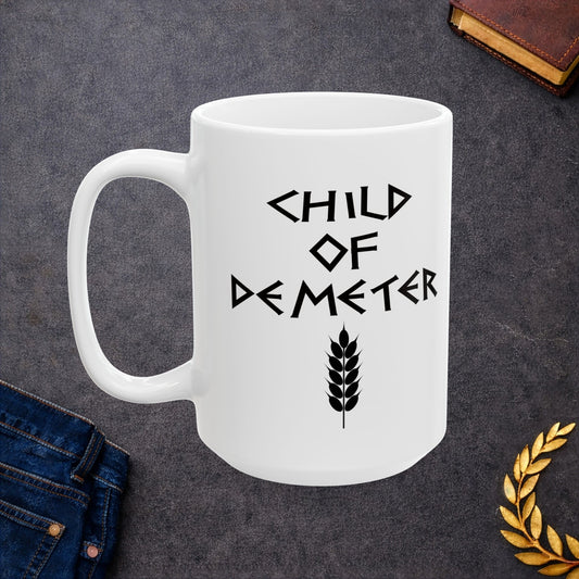 White ceramic mug featuring a minimalist, Greek-inspired graphic in black ink on a white background. The design reads 'CHILD OF DEMETER' in a stylized, angular font, positioned above a clean, line-art graphic of a bundle of harvested wheat.