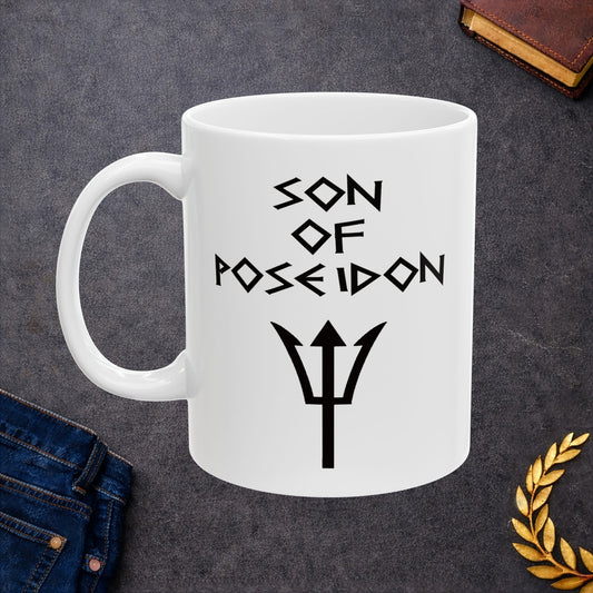 A minimalist black graphic for a white ceramic mug featuring a central silhouette of a trident. Above the trident, the text "SON OF POSEIDON" is written in a sharp, angular font reminiscent of ancient Greek epigraphy. The entire design is rendered in a clean, high-contrast black style.