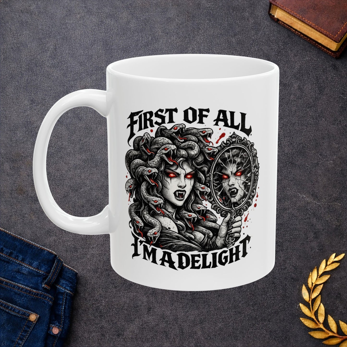 Gothic streetwear illustration of Medusa on a ceramic white mug. Black and white engraving features the figure with serpents for hair, each snake with glowing red eyes. She holds an ornate mirror reflecting her fierce expression with matching red-eyed gaze. Text reads 'First of All, I'm A Delight' in bold metal lettering. Red accents highlight the snakes' eyes. Clever wordplay blends mythology with modern sarcastic humor and confidence.