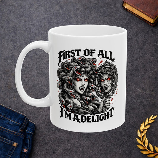 Gothic streetwear illustration of Medusa on a ceramic white mug. Black and white engraving features the figure with serpents for hair, each snake with glowing red eyes. She holds an ornate mirror reflecting her fierce expression with matching red-eyed gaze. Text reads 'First of All, I'm A Delight' in bold metal lettering. Red accents highlight the snakes' eyes. Clever wordplay blends mythology with modern sarcastic humor and confidence.