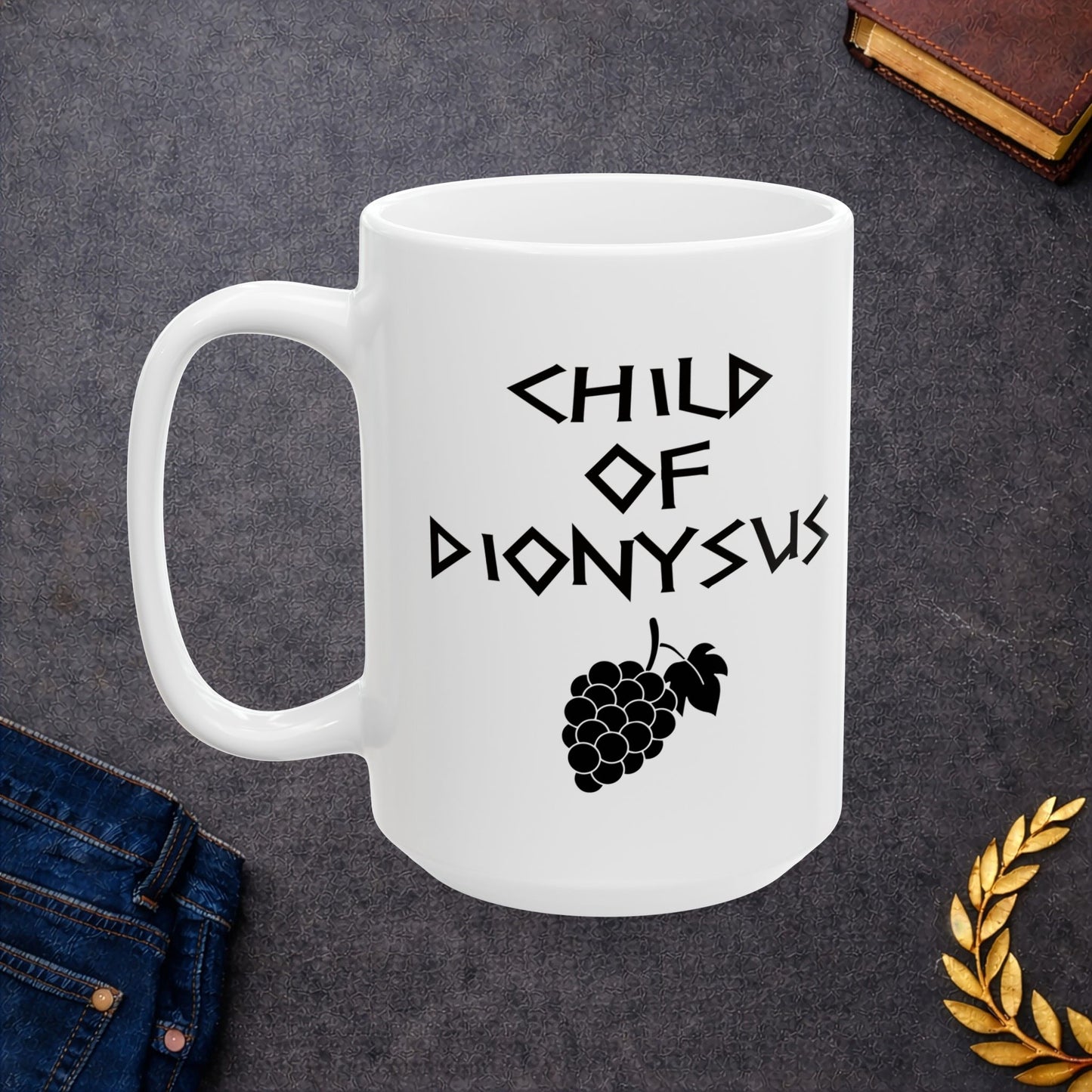 White ceramic mug featuring a minimalist, Greek-inspired graphic in black ink on a white background. The design reads 'CHILD OF DIONYSUS' in a stylized, angular font, positioned above a clean, line-art graphic of a cluster of grapes hanging from a vine with leaves.