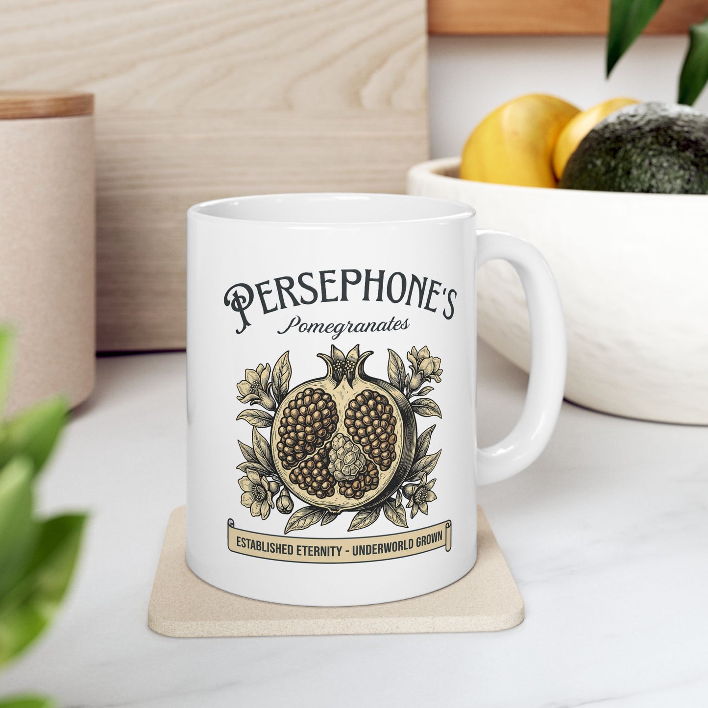 White ceramic mug with a vintage-style botanical illustration of a halved pomegranate showing its seeds, surrounded by delicate pomegranate flowers and leaves. Above the fruit, the text "PERSEPHONE'S Pomegranates" is written in a mix of serif and script fonts. A banner at the bottom reads "ESTABLISHED ETERNITY - UNDERWORLD GROWN." The design features an elegant, woodcut aesthetic in muted earthy tones.
