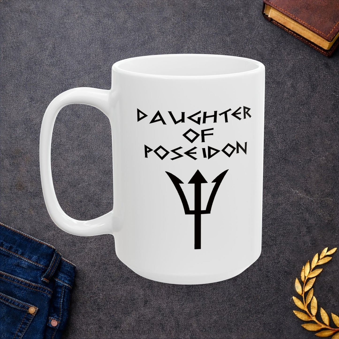 A minimalist black graphic for a white ceramic mug featuring a central silhouette of a trident. Above the trident, the text "DAUGHTER OF POSEIDON" is written in a sharp, angular font reminiscent of ancient Greek epigraphy. The entire design is rendered in a clean, high-contrast black style.