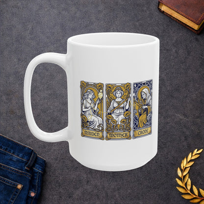 White ceramic mug with Three tarot-style cards depicting the triple goddess archetype: Maiden, Mother, and Crone. The maiden holds a bow surrounded by yellow poppies, the mother wears a crown with a sword, and the crone wears hooded robes with a staff. Each rendered in Art Nouveau style with ornate decorative borders, gold halos, and floral flourishes. Labels appear at card bases. Celebrates the feminine divine in all life stages and cyclical transformation.
