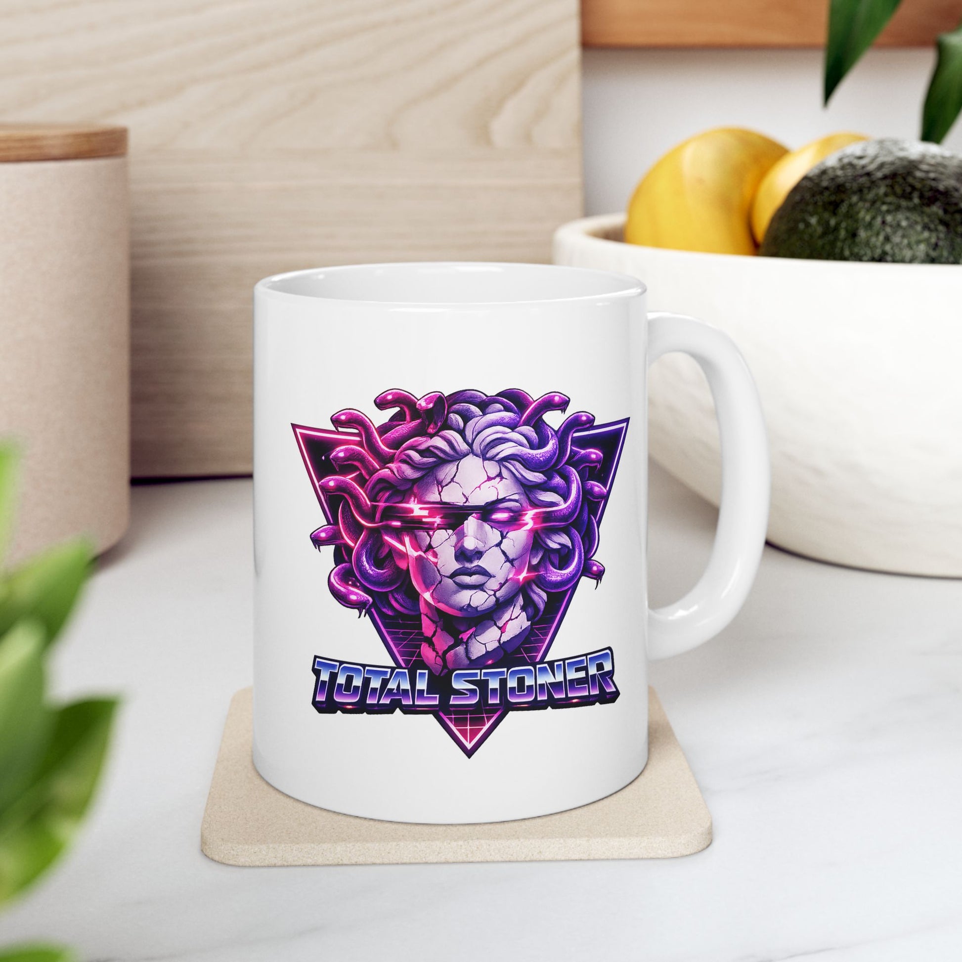White ceramic mug with a synthwave-inspired graphic of Medusa with purple snakes for hair and a cracked stone face. Glowing pink light emanates from her eyes and cracks. The head is centered over a neon pink and purple triangle with a retro grid. Below, the pun "TOTAL STONER" is written in a 1980s-style chrome font with blue and pink gradients. The design uses high-contrast, vibrant neon colors on a dark background.