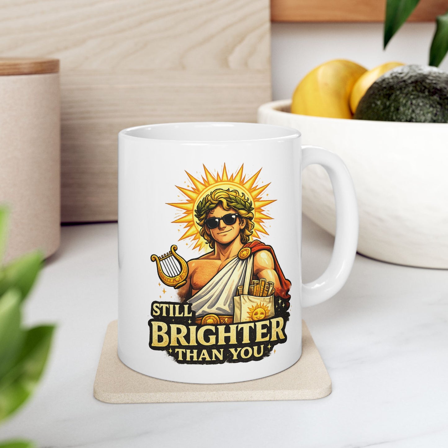 White ceramic mug with a humorous, vibrant illustration of the Greek god Apollo wearing dark sunglasses and a laurel wreath, with a glowing golden sunburst behind his head. He holds a golden lyre and wears a toga with a red cape. Below the smirking god, the cheeky text reads "STILL BRIGHTER THAN YOU" in a bold, weathered yellow font.