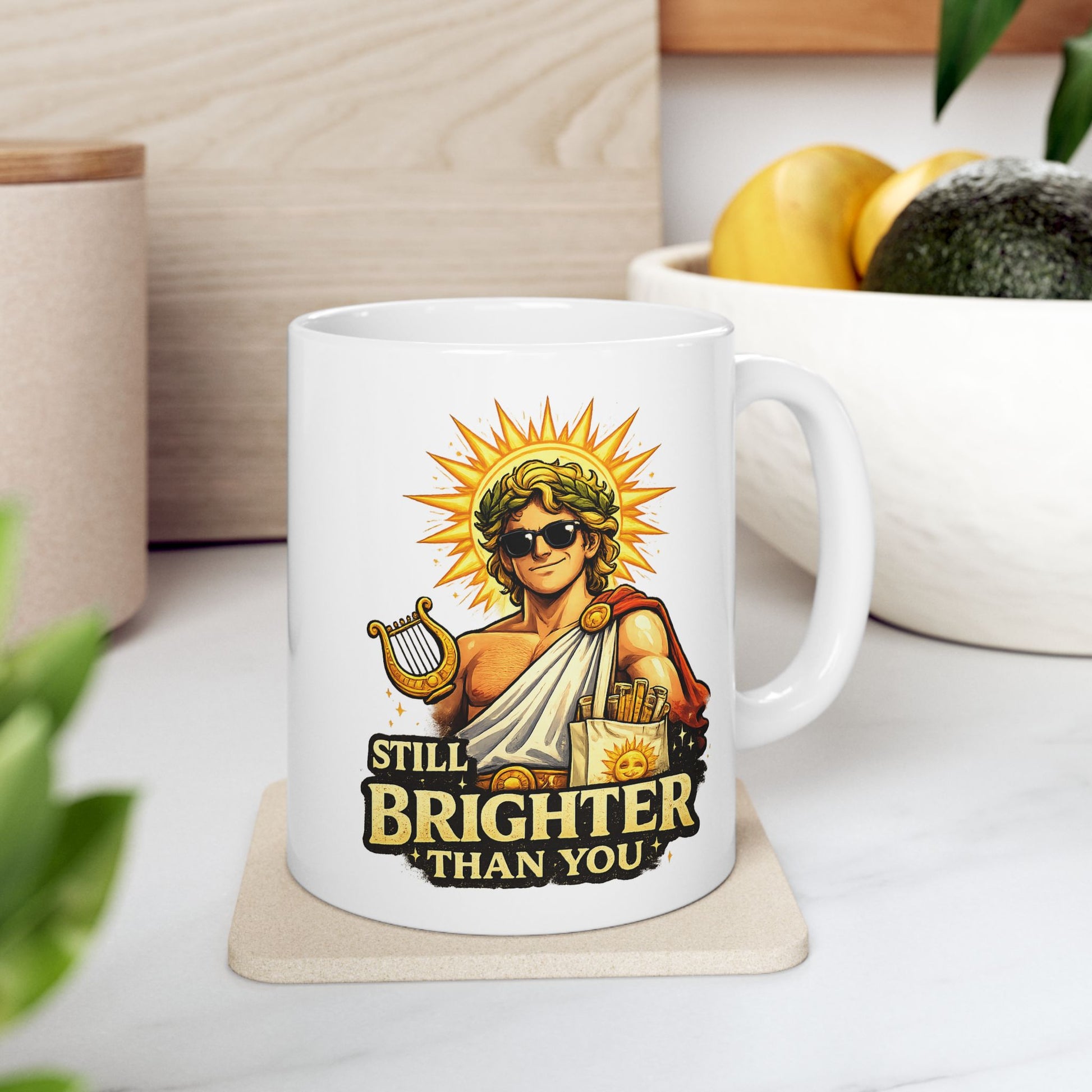White ceramic mug with a humorous, vibrant illustration of the Greek god Apollo wearing dark sunglasses and a laurel wreath, with a glowing golden sunburst behind his head. He holds a golden lyre and wears a toga with a red cape. Below the smirking god, the cheeky text reads "STILL BRIGHTER THAN YOU" in a bold, weathered yellow font.