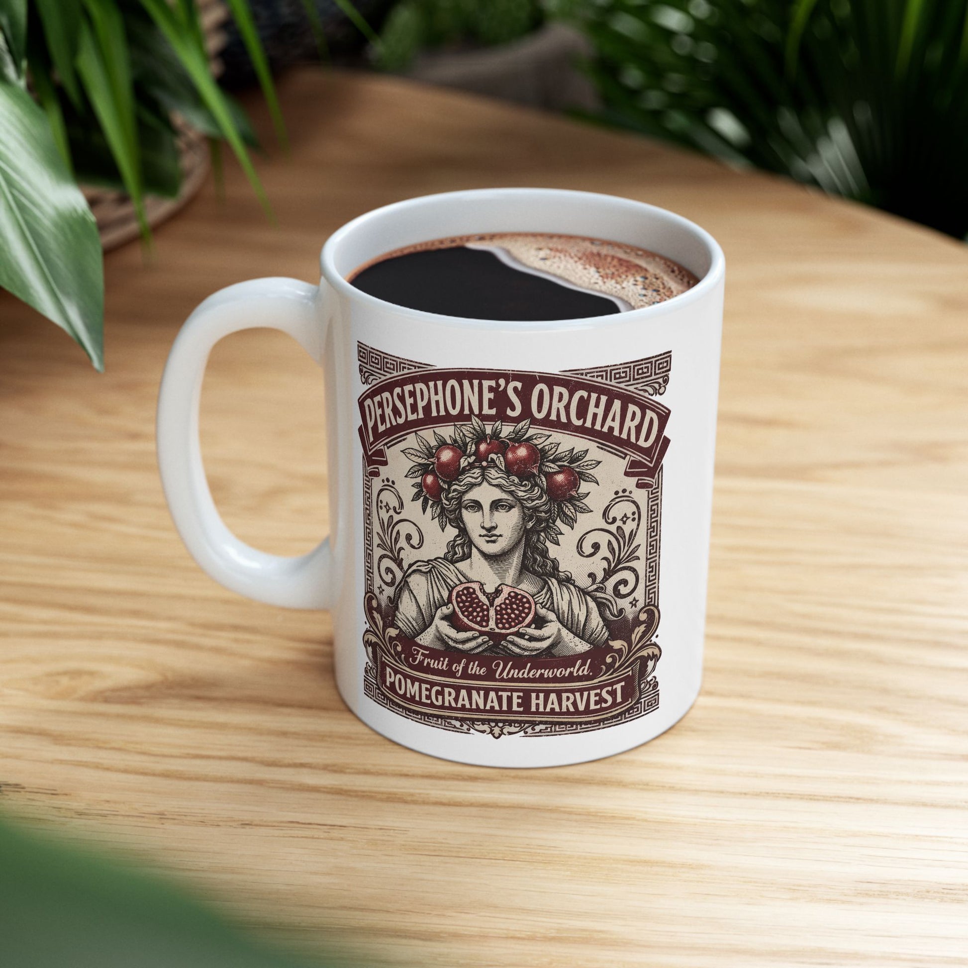 White ceramic mug with a vintage botanical-style illustration of the goddess Persephone, crowned with pomegranates and holding a halved pomegranate revealing its seeds. The artwork is framed by Greek key borders and floral scrolls in a deep burgundy hue. Banners above and below read "PERSEPHONE'S ORCHARD," "Fruit of the Underworld," and "POMEGRANATE HARVEST." The design has an elegant, aged-label aesthetic