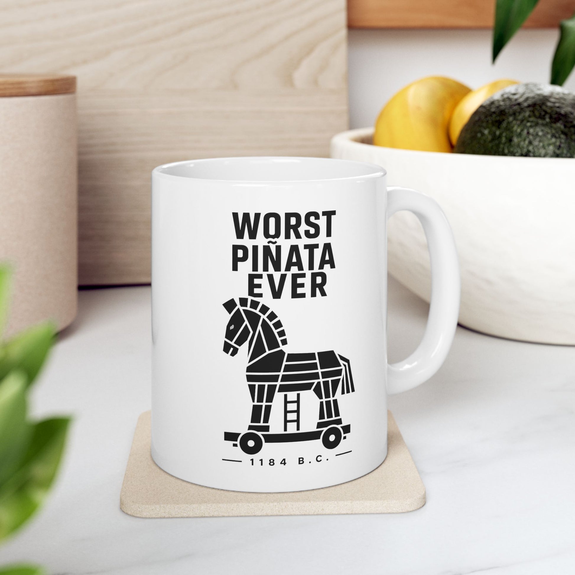 White ceramic mug with a minimalist black-and-white graphic featuring a stylized, geometric silhouette of the Trojan Horse on a wheeled platform with a small ladder underneath. Stacked above the horse, bold black text reads "WORST PIÑATA EVER." Centered below the wheels, a sub-caption reads "— 1184 B.C. —" framed by thin horizontal lines. The clean, high-contrast design offers a humorous, modern take on the ancient Greek myth.