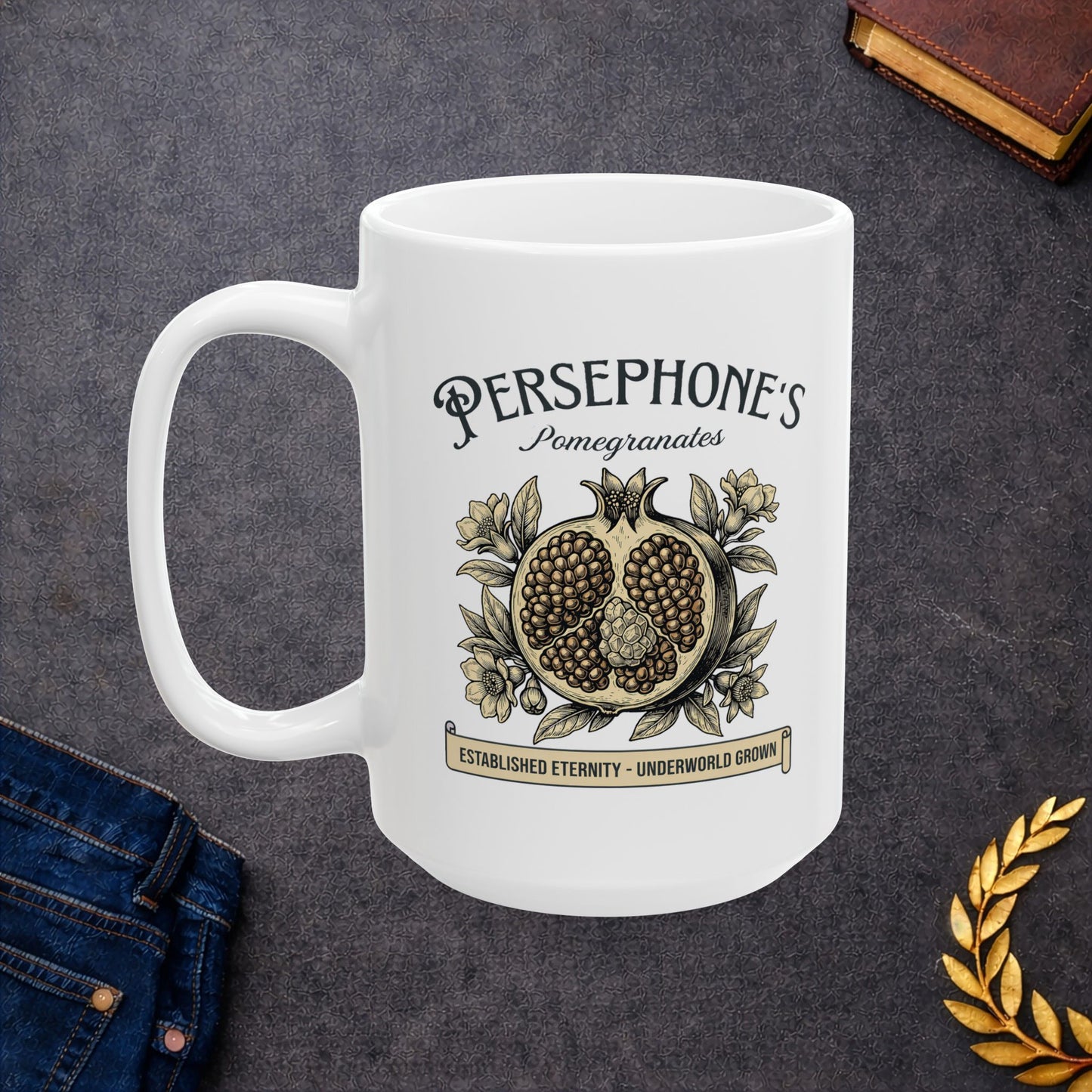 White ceramic mug with a vintage-style botanical illustration of a halved pomegranate showing its seeds, surrounded by delicate pomegranate flowers and leaves. Above the fruit, the text "PERSEPHONE'S Pomegranates" is written in a mix of serif and script fonts. A banner at the bottom reads "ESTABLISHED ETERNITY - UNDERWORLD GROWN." The design features an elegant, woodcut aesthetic in muted earthy tones.
