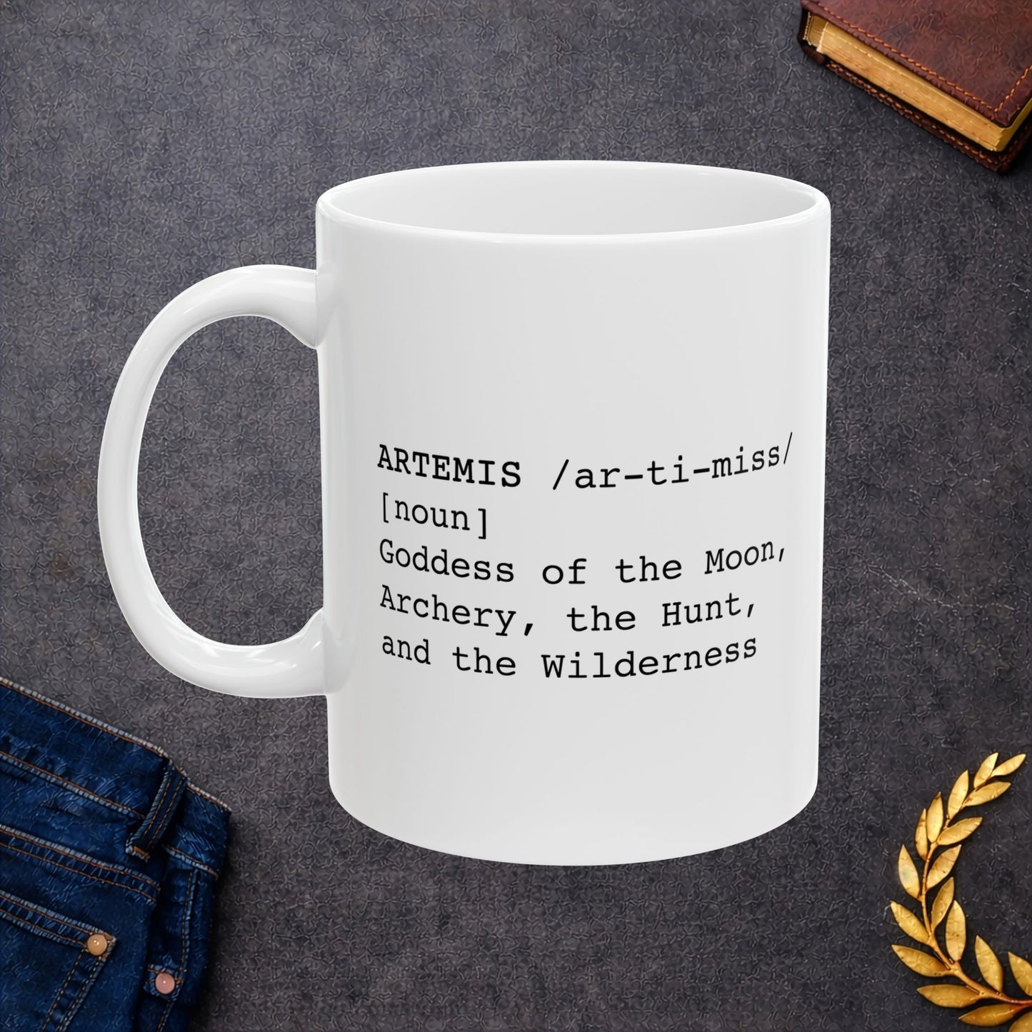 White ceramic mug featuring a dictionary-style definition graphic in black text on a white background. The text reads: 'ARTEMIS /ar-ti-miss/ [noun] Goddess of the Moon, Archery, the Hunt, and the Wilderness.'