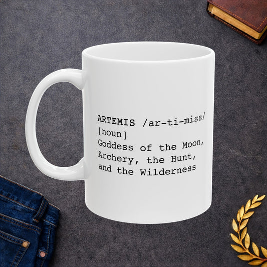 White ceramic mug featuring a dictionary-style definition graphic in black text on a white background. The text reads: 'ARTEMIS /ar-ti-miss/ [noun] Goddess of the Moon, Archery, the Hunt, and the Wilderness.'