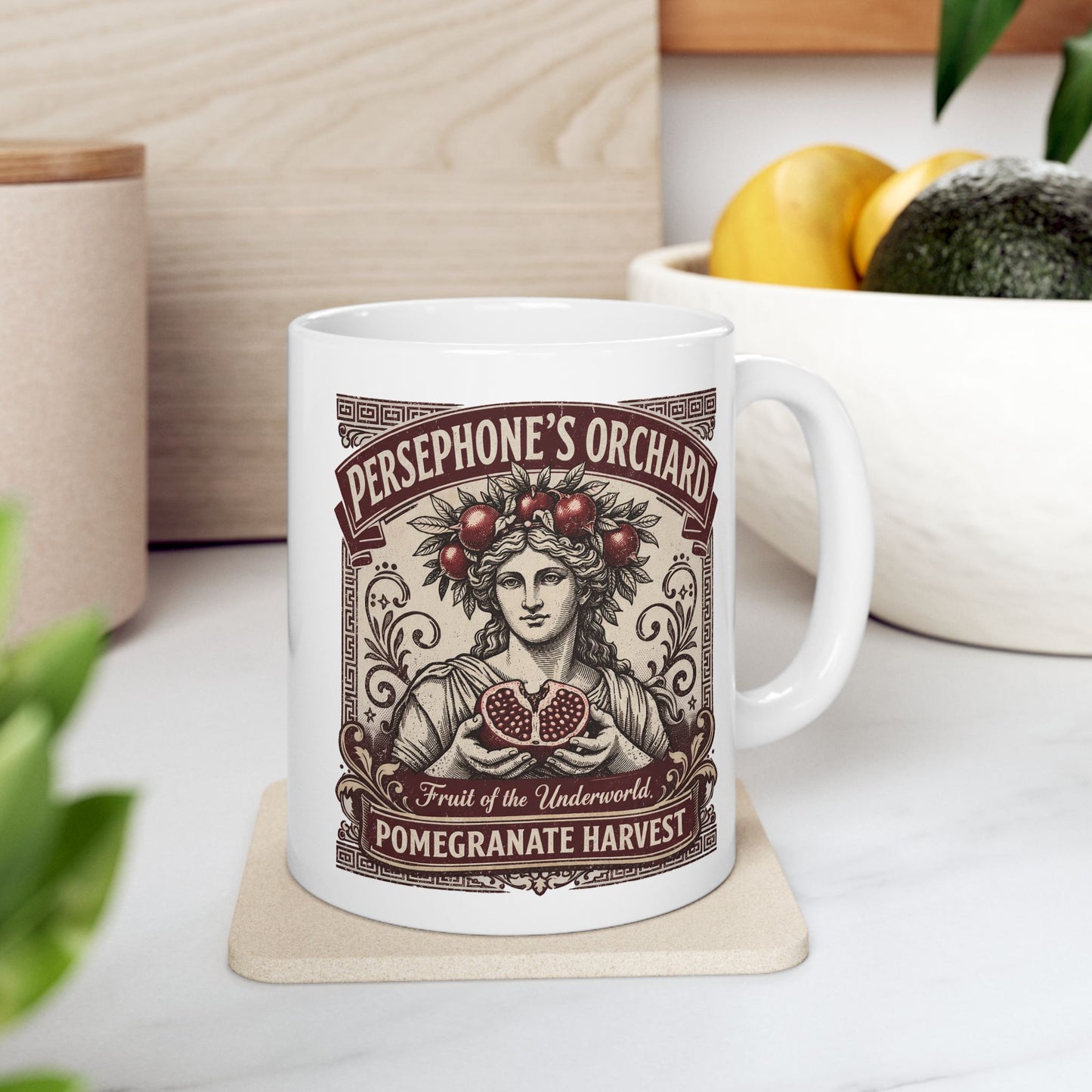 White ceramic mug with a vintage botanical-style illustration of the goddess Persephone, crowned with pomegranates and holding a halved pomegranate revealing its seeds. The artwork is framed by Greek key borders and floral scrolls in a deep burgundy hue. Banners above and below read "PERSEPHONE'S ORCHARD," "Fruit of the Underworld," and "POMEGRANATE HARVEST." The design has an elegant, aged-label aesthetic