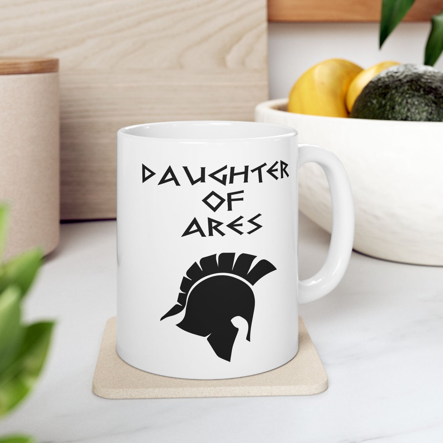 White ceramic mug featuring a minimalist, Greek-inspired graphic in black ink on a white background. The design reads 'DAUGHTER OF ARES' in a stylized, angular font, positioned above a clean, line-art graphic of a Spartan-style plumed warrior helmet.
