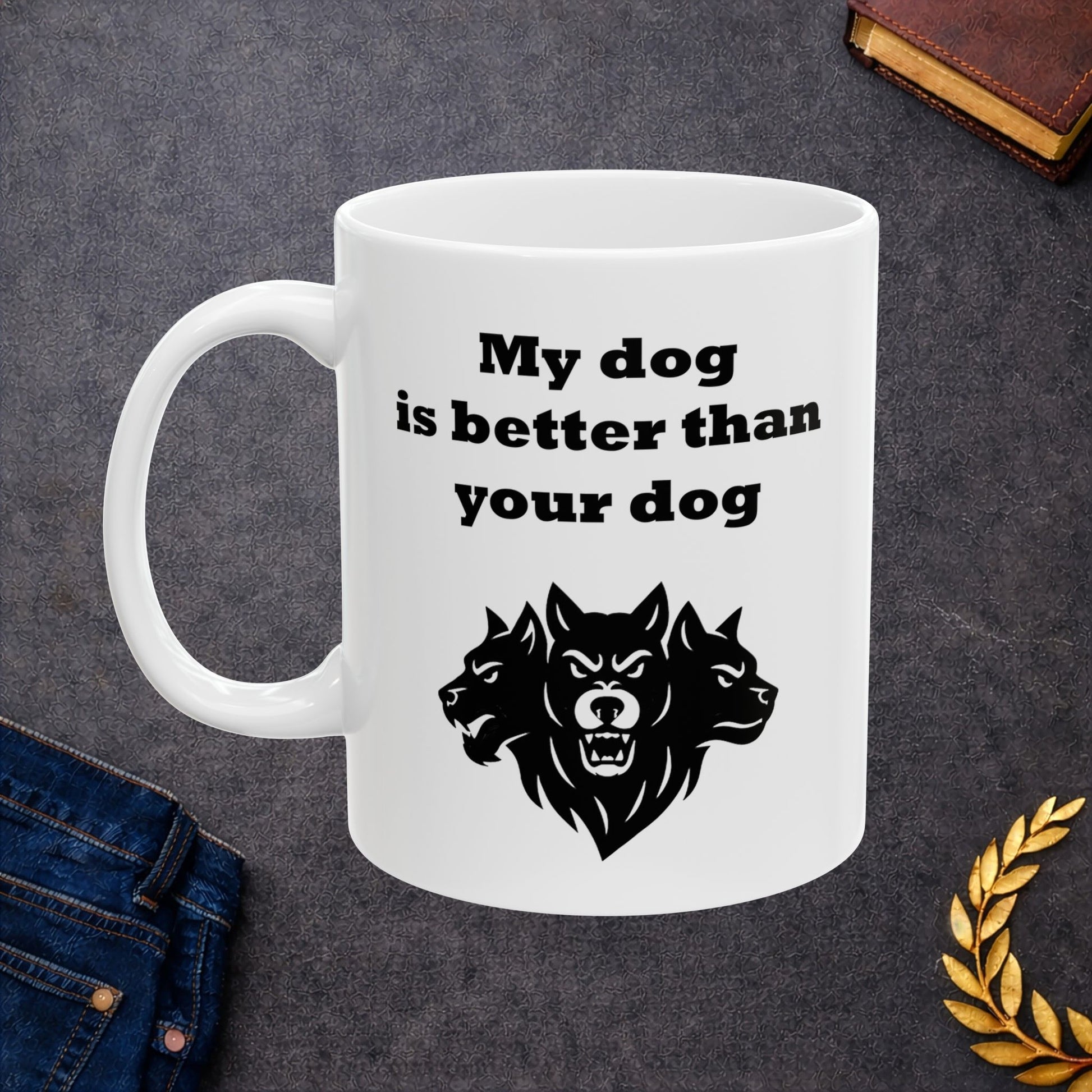 White ceramic mug with a minimalist black-and-white graphic featuring a bold, three-headed Cerberus illustration. The hound of the underworld is shown with snarling expressions and sharp teeth. Above the heads, the phrase "My dog is better than your dog" is written in a heavy, black slab-serif font. The design is a clean, modern take on Greek mythology with a humorous twist.