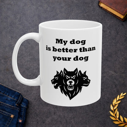 White ceramic mug with a minimalist black-and-white graphic featuring a bold, three-headed Cerberus illustration. The hound of the underworld is shown with snarling expressions and sharp teeth. Above the heads, the phrase "My dog is better than your dog" is written in a heavy, black slab-serif font. The design is a clean, modern take on Greek mythology with a humorous twist.