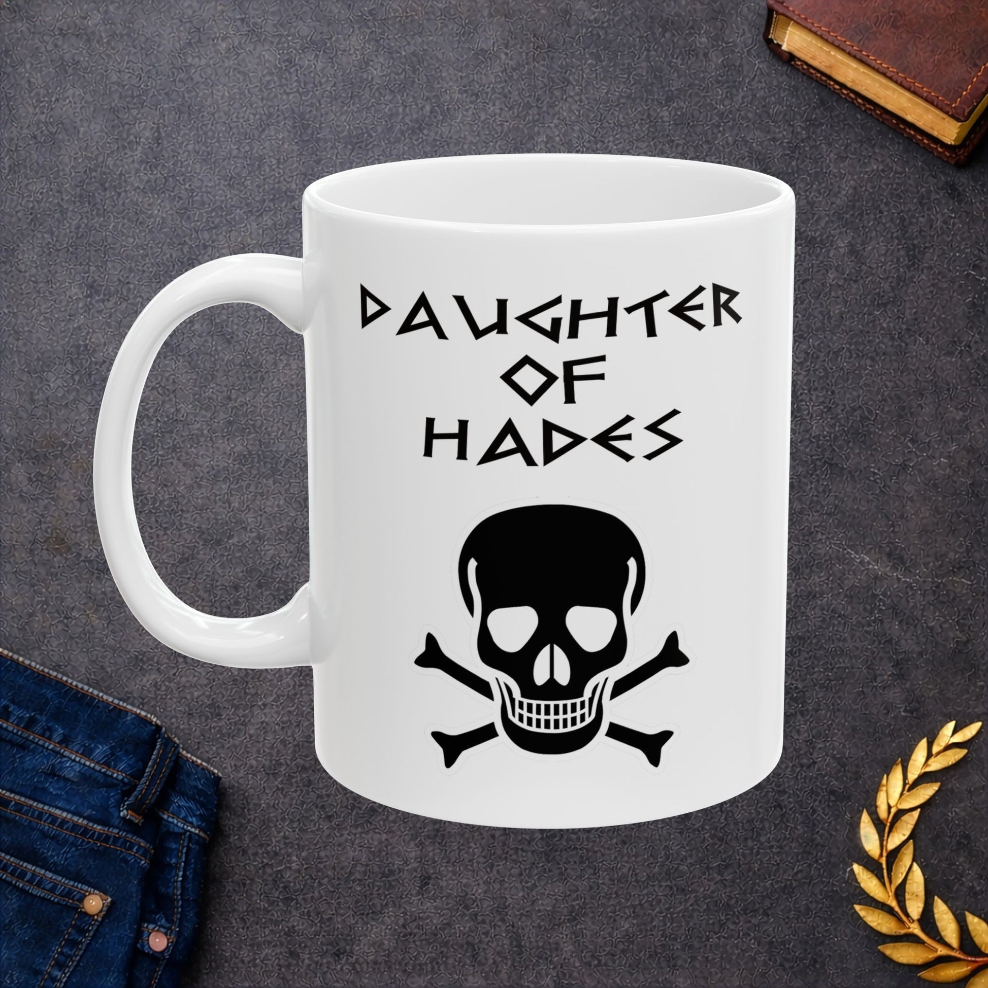 A bold, dark-themed graphic for a white ceramic mug. The design features a large, detailed outline of a skull and crossbones at the center. Above the skull, the words "DAUGHTER OF HADES" are written in a sharp, ancient Greek-inspired angular font. The entire design is rendered in a clean, high-contrast black outline style.