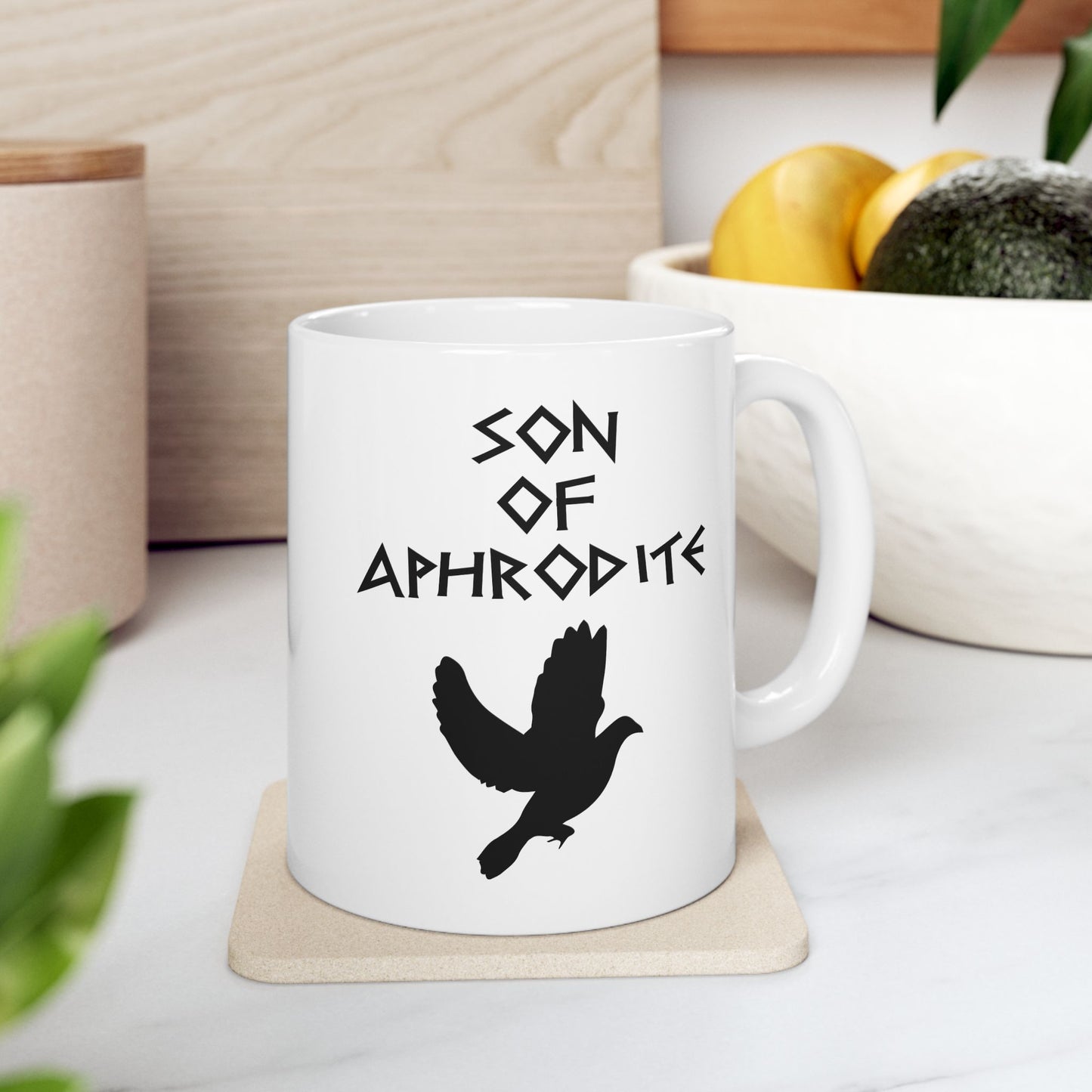 White ceramic mug featuring a minimalist, Greek-inspired graphic in black ink on a white background. The design reads 'SON OF APHRODITE' in a stylized, angular font, positioned above a clean, line-art graphic of a dove in flight.