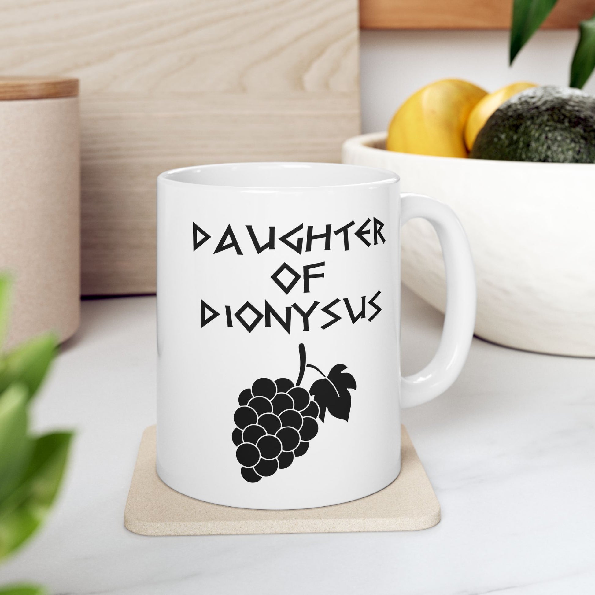 White ceramic mug featuring a minimalist, Greek-inspired graphic in black ink on a white background. The design reads 'DAUGHTER OF DIONYSUS' in a stylized, angular font, positioned above a clean, line-art graphic of a cluster of grapes hanging from a vine with leaves.