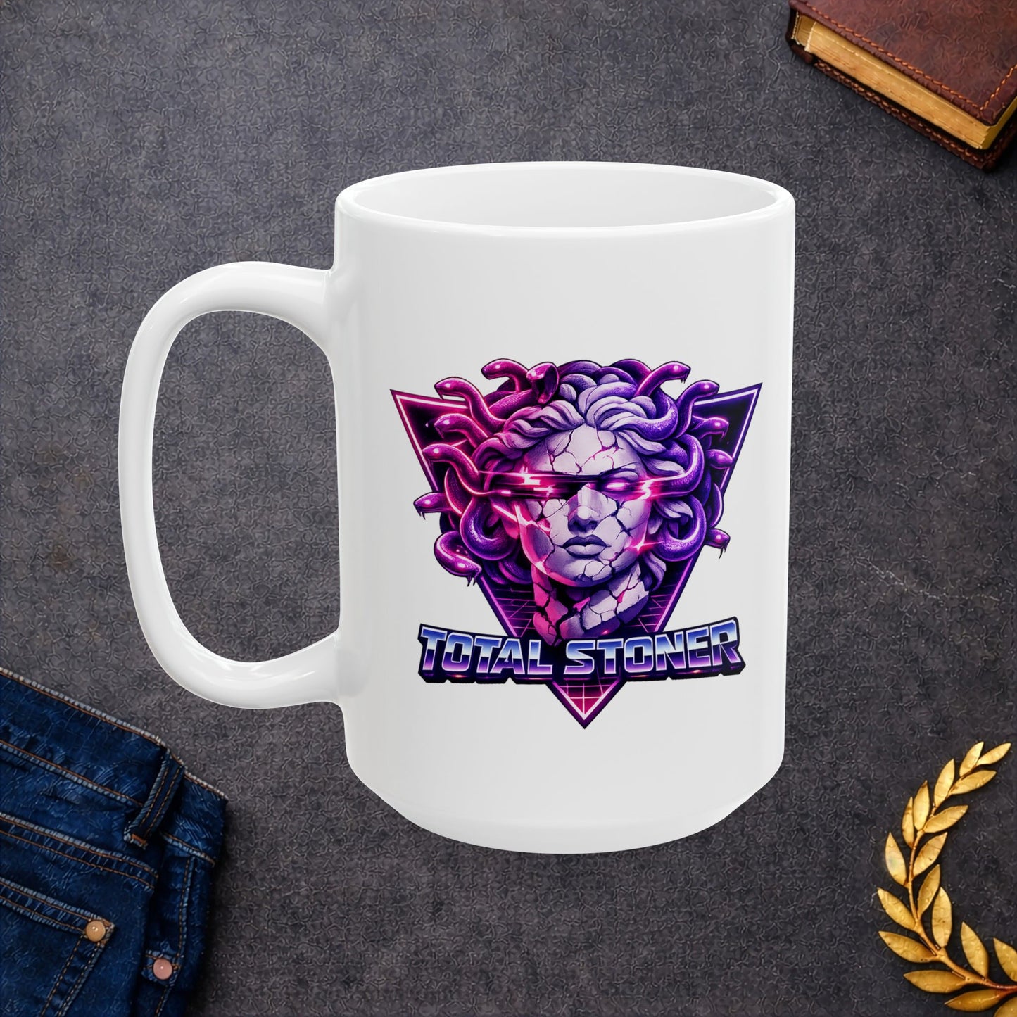 White ceramic mug with a synthwave-inspired graphic of Medusa with purple snakes for hair and a cracked stone face. Glowing pink light emanates from her eyes and cracks. The head is centered over a neon pink and purple triangle with a retro grid. Below, the pun "TOTAL STONER" is written in a 1980s-style chrome font with blue and pink gradients. The design uses high-contrast, vibrant neon colors on a dark background.